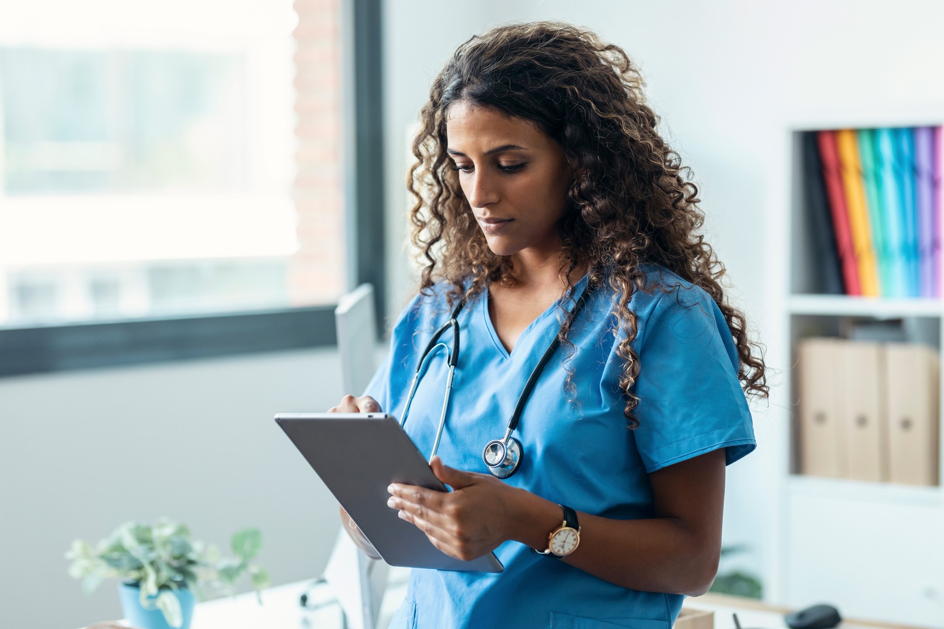 Female nurse using her digital tablet while standing in the consultation.